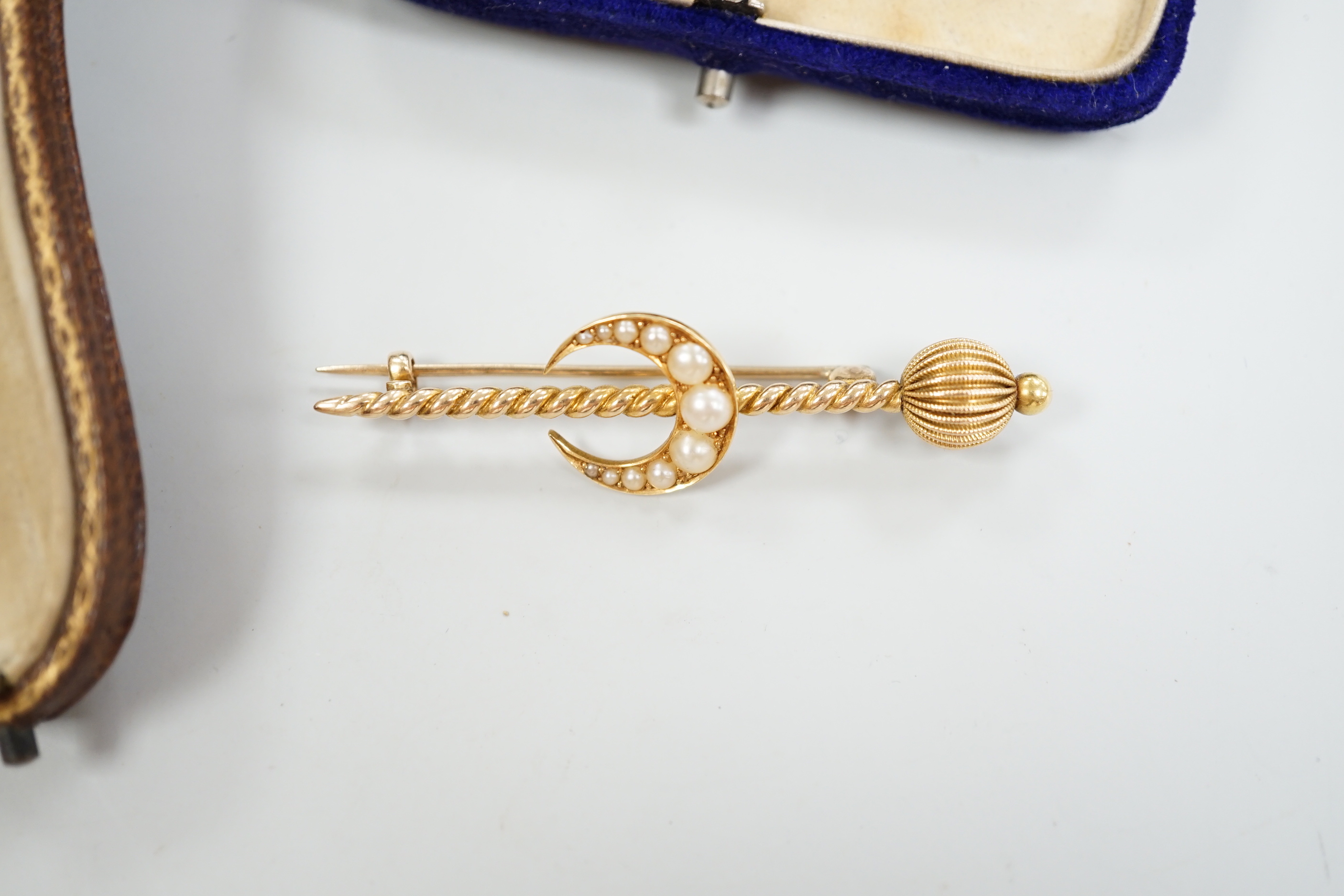 An Edwardian enamel and diamond set 'horse and jockey' stick pin, 63mm, a yellow metal and seed pearl set 'crescent and staff, brooch and a 'riding crop and horseshoe' brooch.